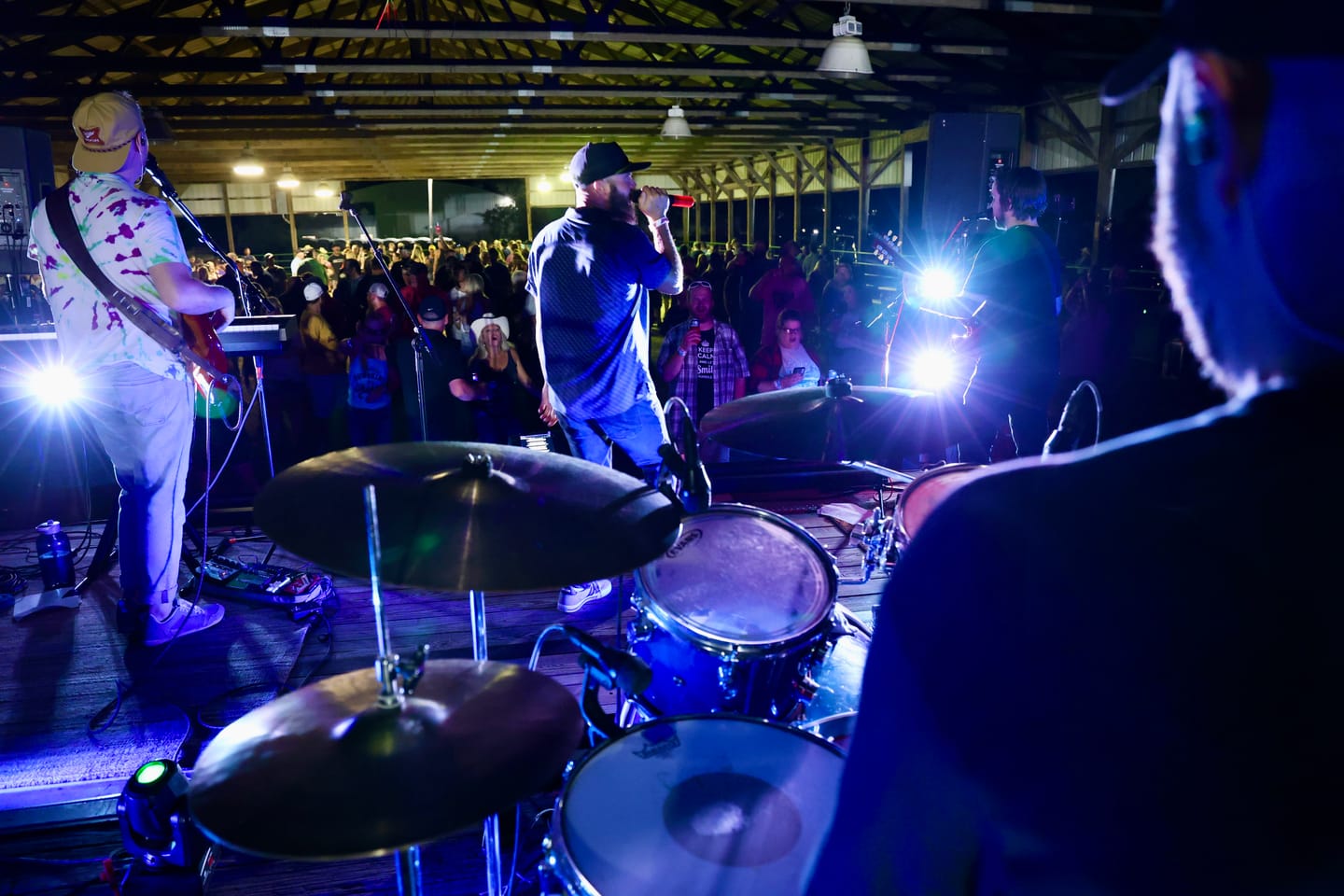 View from behind the drum kit as the singer works a crowd gathered under an open-air pavilion