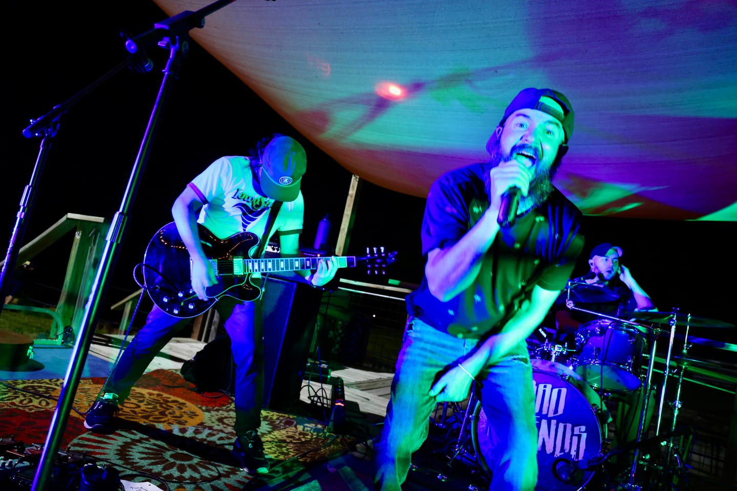Bad Friends' singer and guitarist under green and purple stage lights, the band's logo on the kick drum