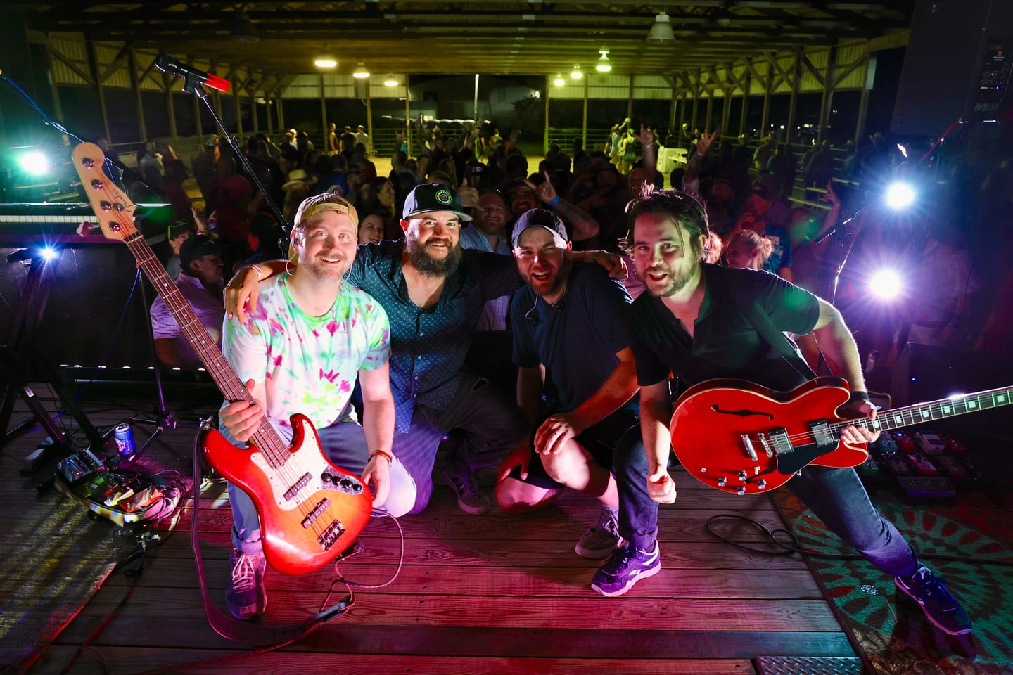 The four members of Bad Friends crouched at the front of a wooden stage with their guitars, crowd behind them