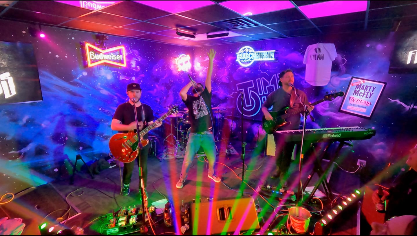 Bad Friends mid-set under neon beer signs and colored stage lasers on a small bar stage