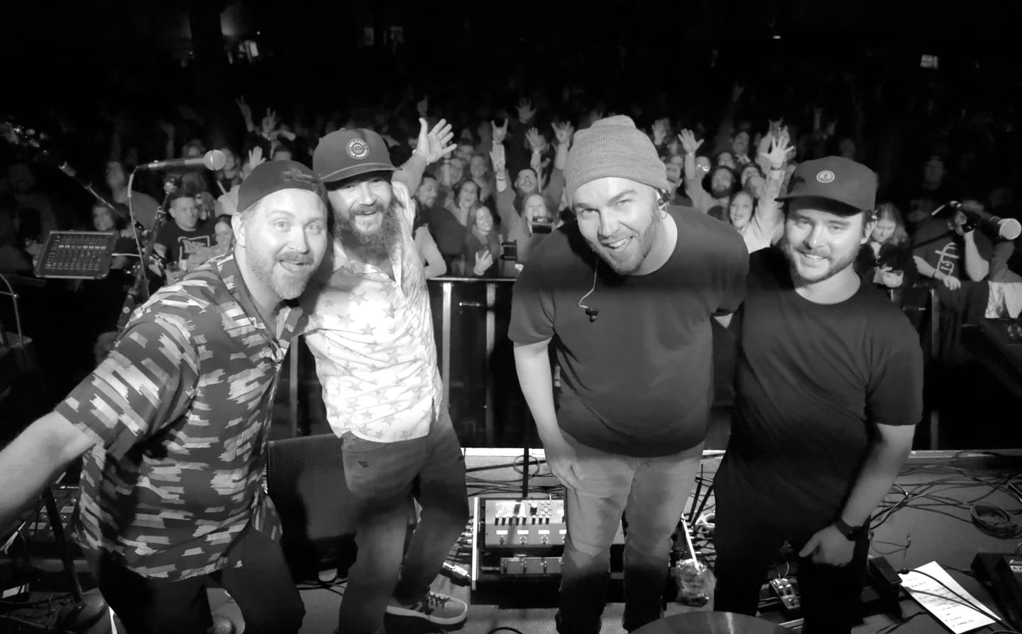 Bad Friends posing together at the front of the stage at Wooly's in Des Moines, a packed crowd cheering with hands raised behind them